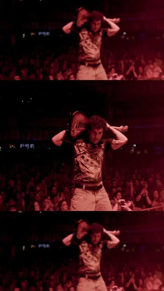 townsend holding his guitar behind his head under red stage light